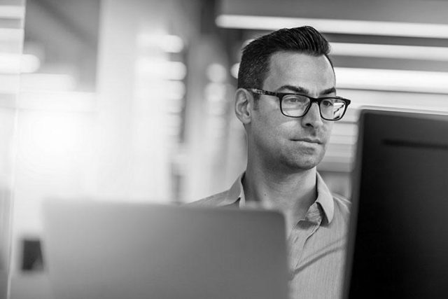 man wearing glasses working on a laptop.